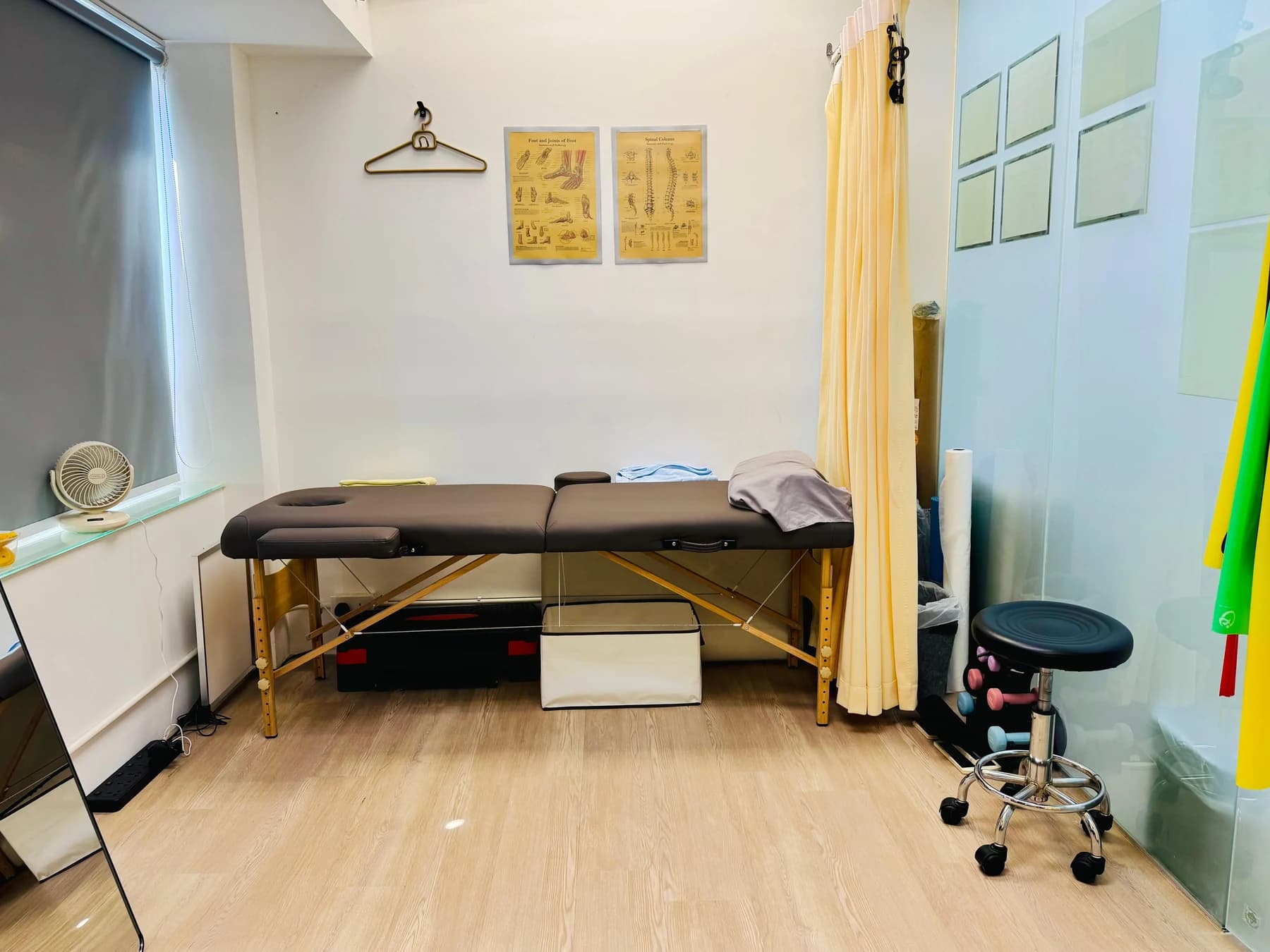 明亮的治療室，設有空置的治療床、私隱拉簾、解剖圖海報及復康器材。